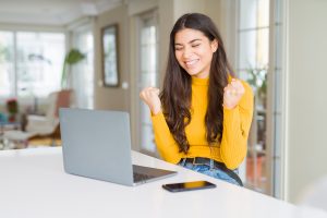 Young woman using computer laptop looking victorious and confident because we can do online therapy in Florida for codependency, self-sabotage, imposter syndrome, divorce recovery and more with online counseling for women with anxiety in Miramar, FL. Meet with online therapist in Florida, Enid.