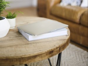 Journal on a table with two plants and a sofa in the background. Learn more about the benefits of journaling for high-performing women for confidence building in Miramar, FL. She gets online therapy in Florida for women with anxiety and codependency and perfectionism.