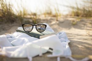 Sunglasses on top of a book on a blanket on the beach in Miramar, FL. You can get codependency counseling for women in Florida with online therapist Enid to talk about setting healthy boundaries in Miramar, FL