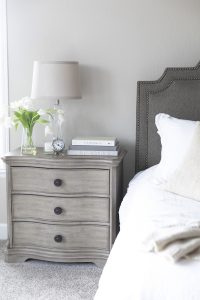 Photo of a bed with grey headboard and grey side table with flowers and books belonging to a woman experiencing dating anxiety in Miramar, FL. You can get online therapy in Florida for codependency and setting boundaries in MIramar, FL from an online therapist who specializes in relationship counseling for singles.