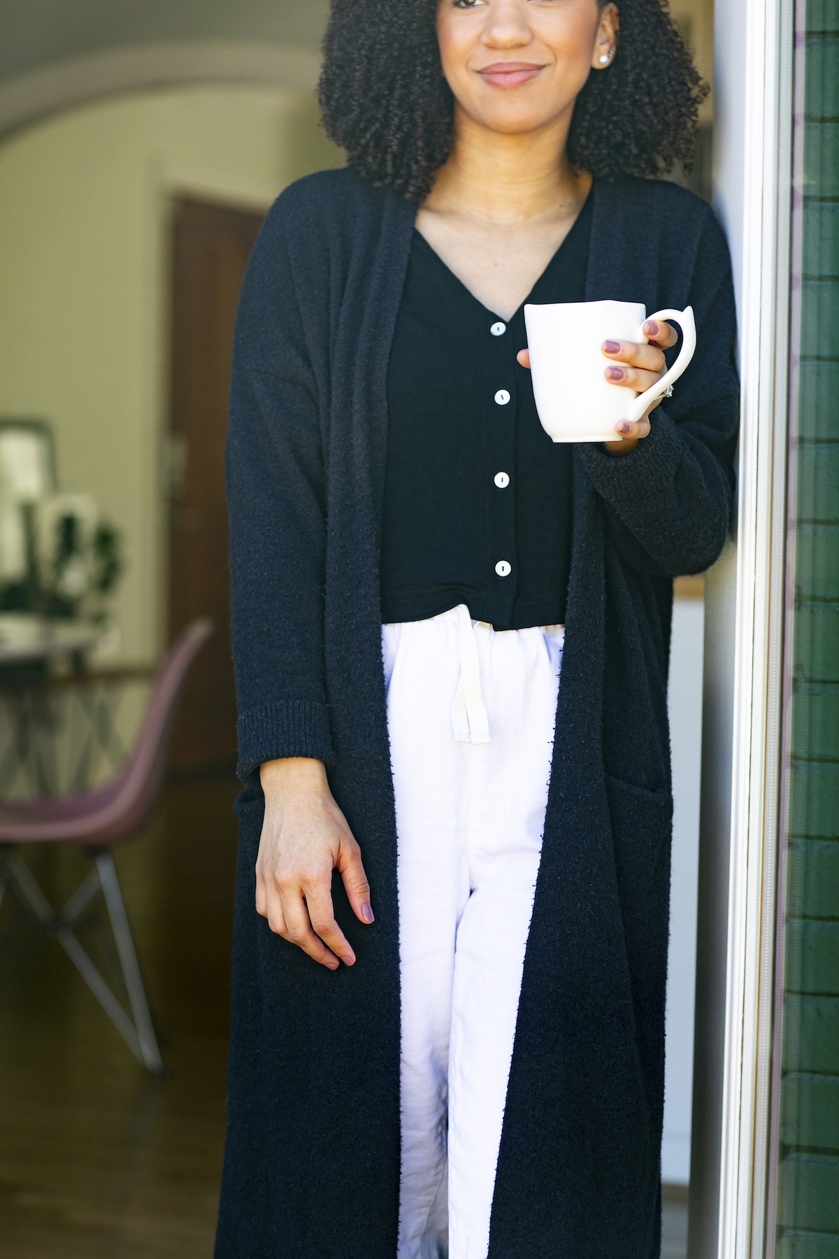 Woman with coffee cup leaning against the wall outside, looking out her front door. A Miramar, FL therapist for women gives tips for a self-compassion practice with perfectionism counseling in Miramar, FL. You can get online therapy in Florida here.