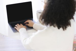 Woman with her back to camera, typing on laptop. A Miramar, FL therapist for women gives tips for a self-compassion practice with perfectionism counseling in Miramar, FL. You can get online therapy in Florida here.