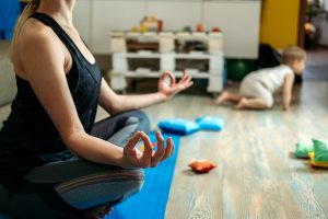Mindfulness meditation concept. Young woman, mother practicing yoga at home sitting in lotus pose, meditating relaxing with closed eyes with baby daughter at home. Support for women in Miramar, FL is here with Broward counselor, Enid. You can get help with online therapy for women in Florida here!