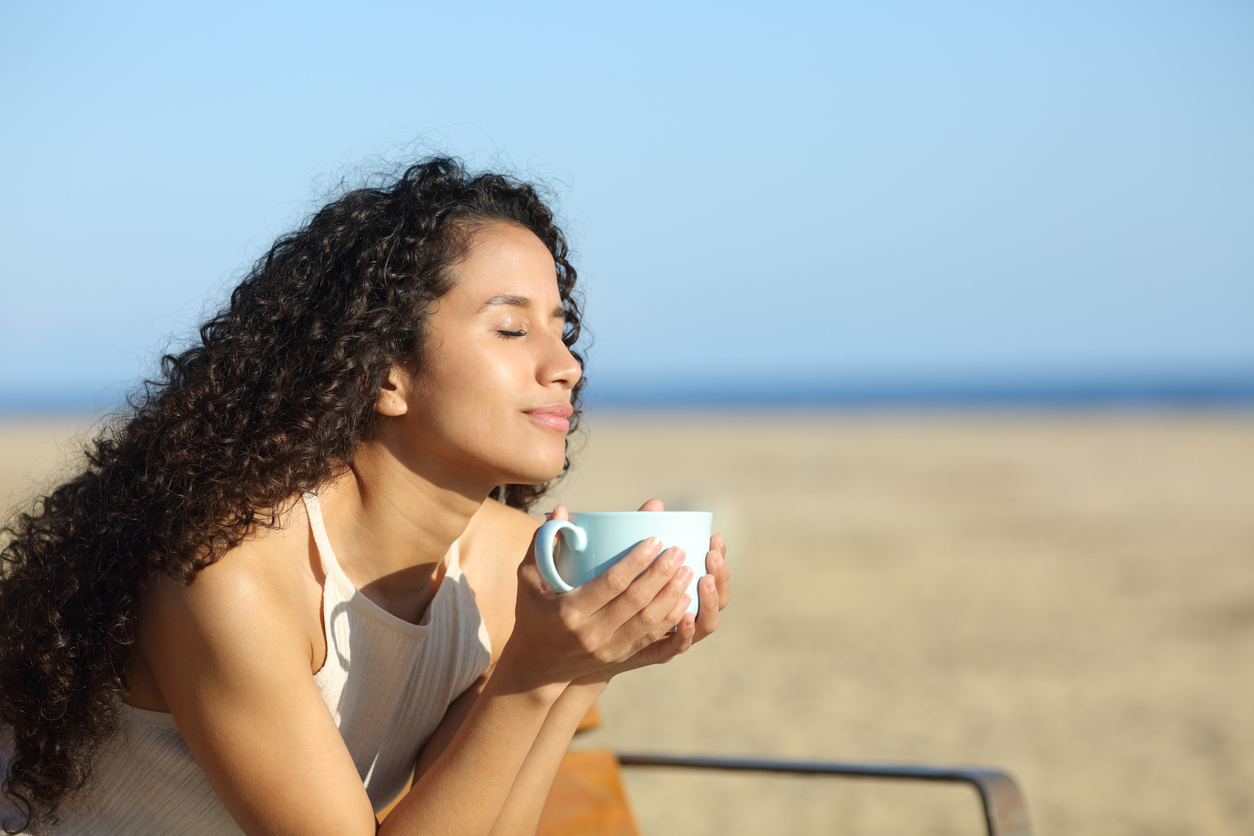 Latin woman enjoying a cup of coffee breathing fresh air on the beach a sunny day. You can get online therapy in florida with support for women in Miramar, FL.