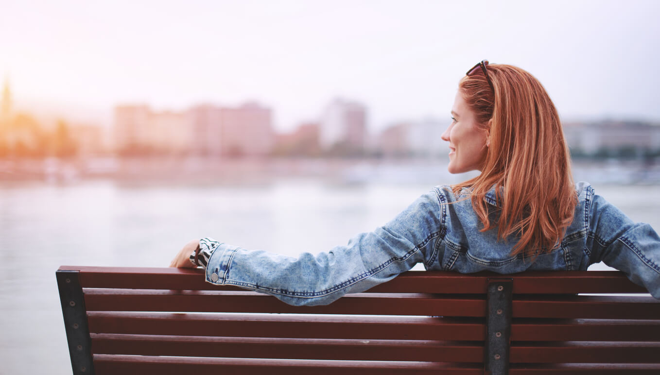Woman sitting on a bench looking over the ocean smiling. HSP women in Florida can learn about anxiety symptoms with Miramar, FL therapist Enid.