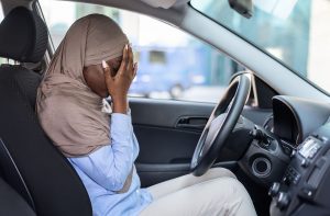 Depressed and stressed black Muslim woman in the car with hands over her face. This person could use anxiety treatment for women in Miramar, FL and beyond with online therapy in Florida for HSP Women.
